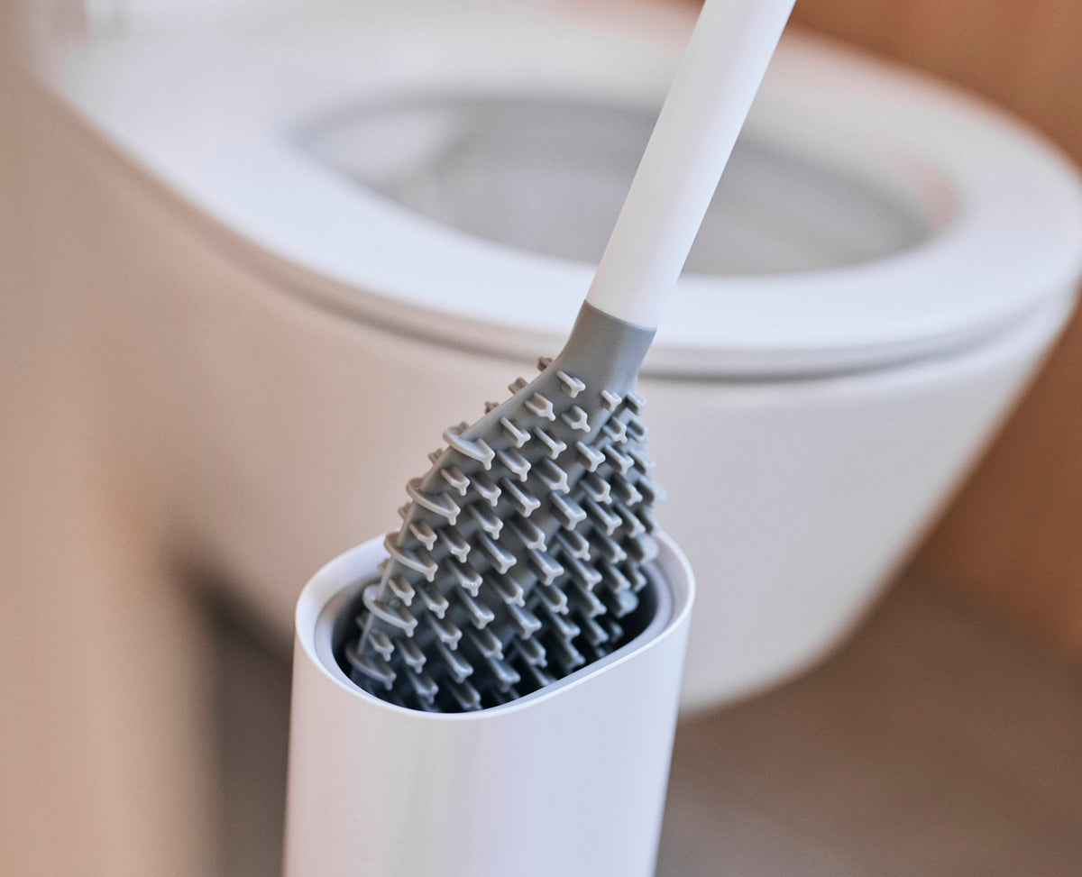 Joseph Joseph Flex TriBlade toilet brush in its fully enclosed holder beside a toilet