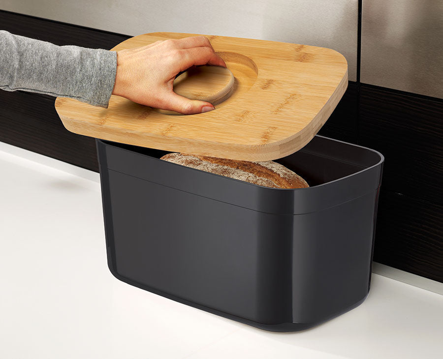 The bamboo lid lifted off the black bread bin to show the storage space inside.