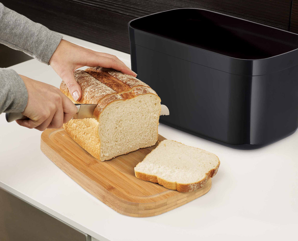 The black bread bin holding loaves and rolls to show its capacity.
