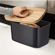 Angled view of the black Joseph Joseph 35 cm melamine bread bin and its beech wood lid.