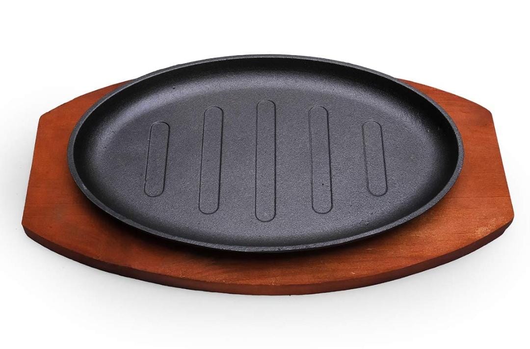 Cast iron hot sizzling plate on wooden tray