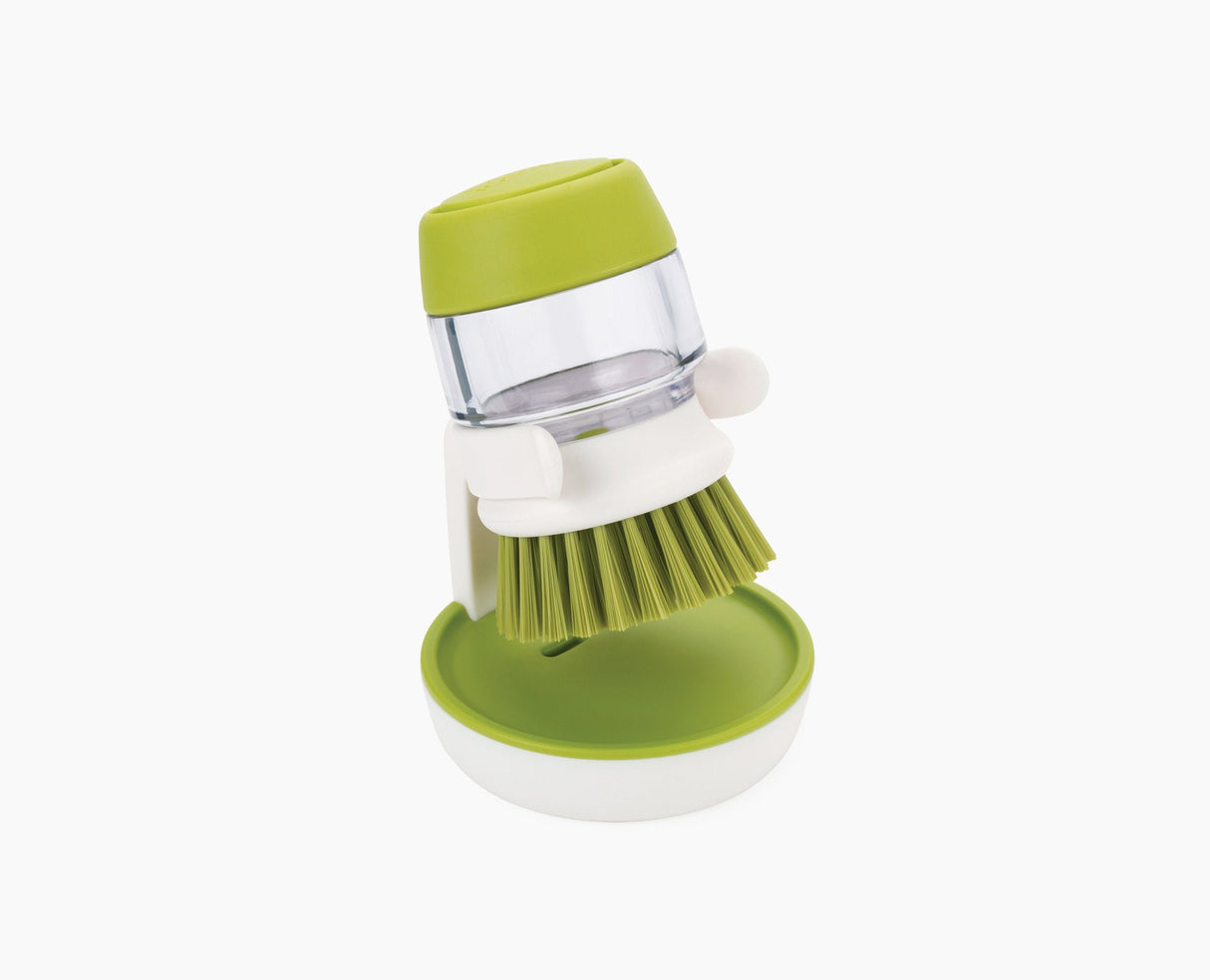 Joseph Joseph Palm Scrub soap-dispensing washing-up brush in green with its storage stand.