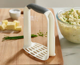 A hand gripping the D-shaped handle to mash inside a pan.