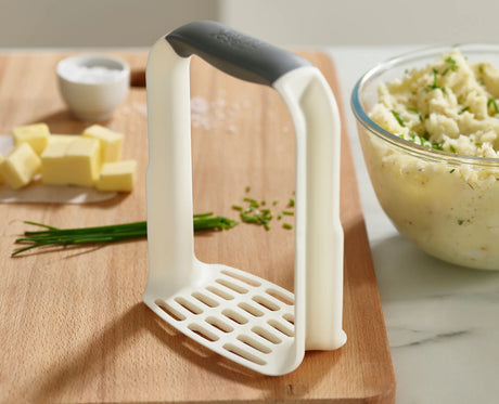 A hand gripping the D-shaped handle to mash inside a pan.