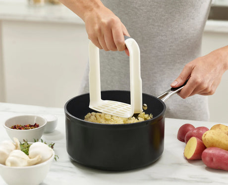The masher's curved edge following the side of a pan while scraping.