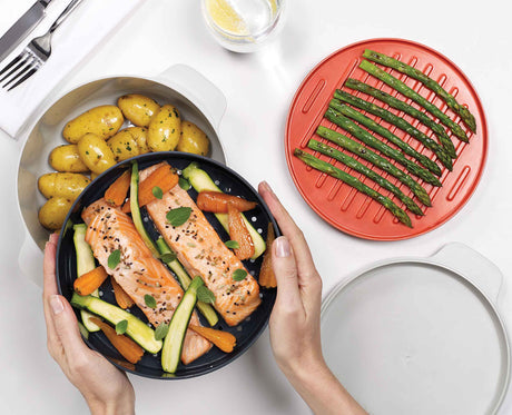 The M-Cuisine set in use cooking a meal, showing the integrated orange handles