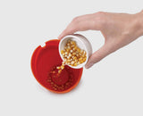 Kernels being poured into the orange silicone popcorn cup
