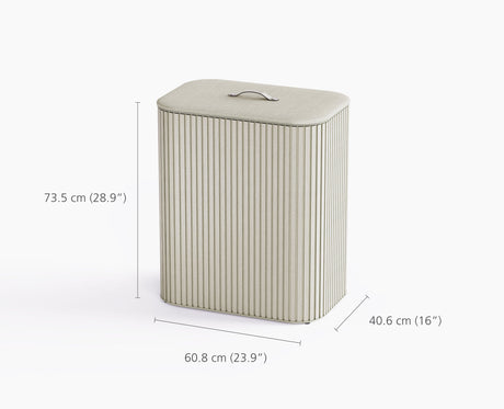 The ecru Tota Luxe laundry basket styled beside a bed in a bedroom setting.