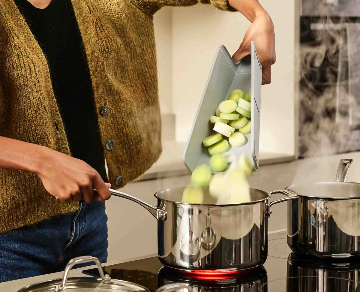 Chopped vegetables being poured from the folded board into a pan.