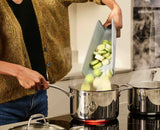 Chopped vegetables being poured from the folded board into a pan.