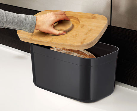 The bamboo lid lifted off the black bread bin to show the storage space inside.