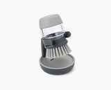 Joseph Joseph Palm Scrub washing-up brush in grey resting on its stand.