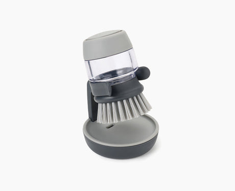 Joseph Joseph Palm Scrub washing-up brush in grey resting on its stand.